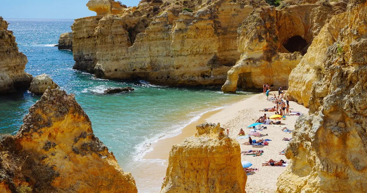 Zandbaai tussen goudgele kliffen aan de Algarve met badgasten op het strand