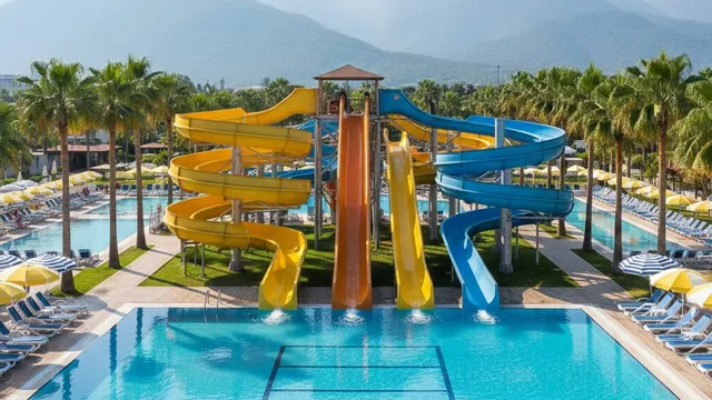 Gele, oranje en blauwe waterglijbanen boven het zwembad van een Turks resort, met de Taurusbergen in de verte