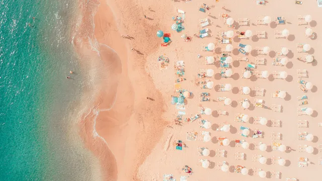 Luchtfoto van een vol zomerstrand met rijen parasols en ligbedden