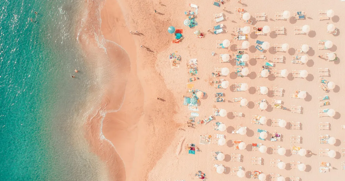 Luchtfoto van een vol zomerstrand met rijen parasols en ligbedden