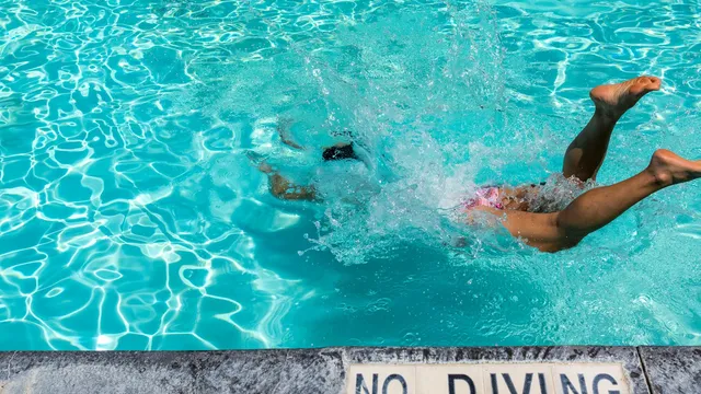 Iemand duikt met een plons in een helderblauw zwembad naast een No Diving-tegel