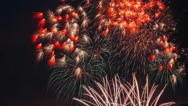 Groot vuurwerk boven een baai met boten en toeschouwers