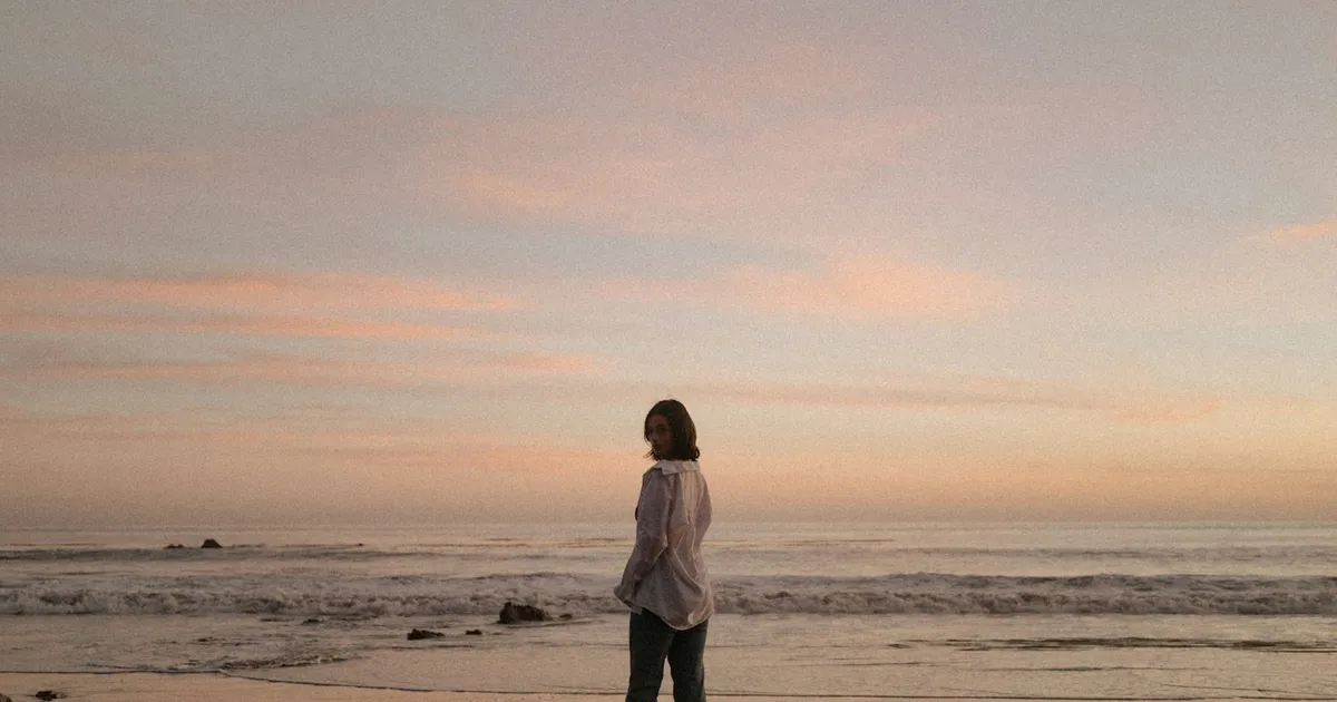 Vrouw staat alleen op het strand bij zonsondergang