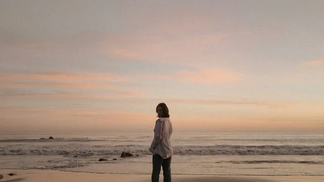Vrouw staat alleen op het strand bij zonsondergang