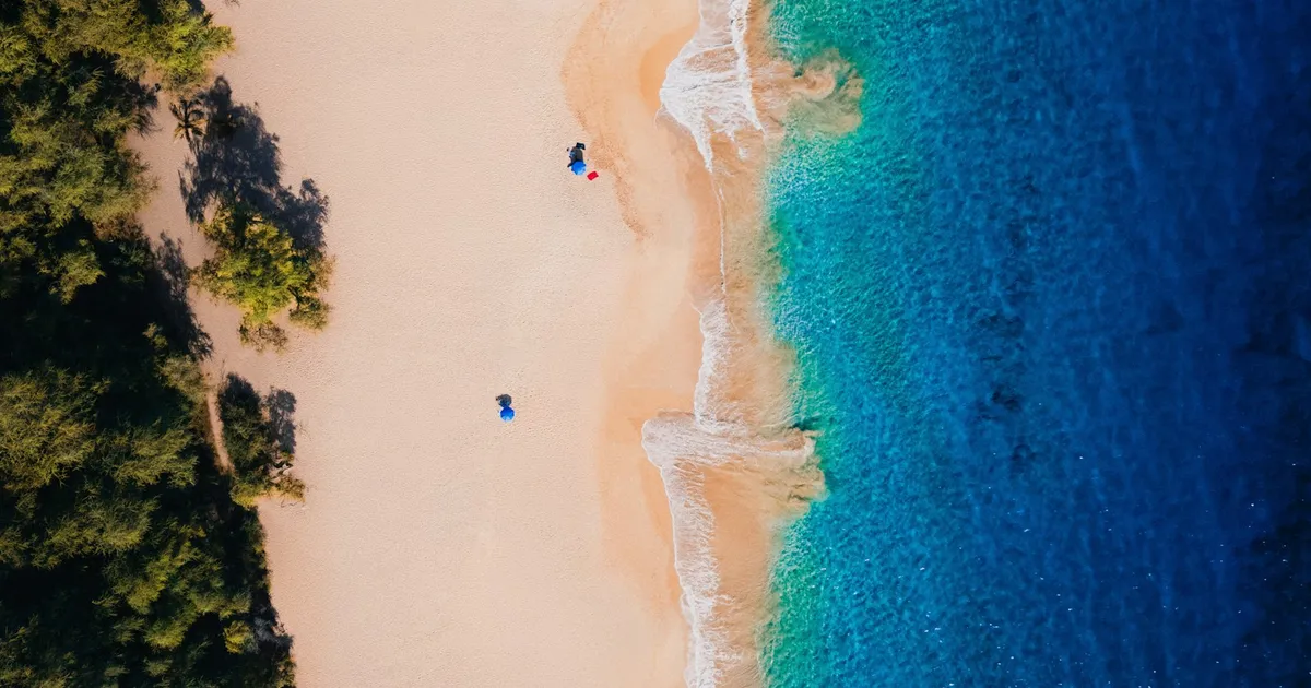 Luchtfoto van een verlaten zandstrand met turquoise zee en groene bomen