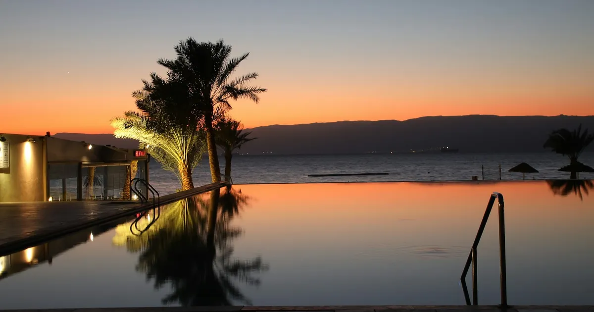 Infinity pool met palmen aan zee tijdens zonsondergang