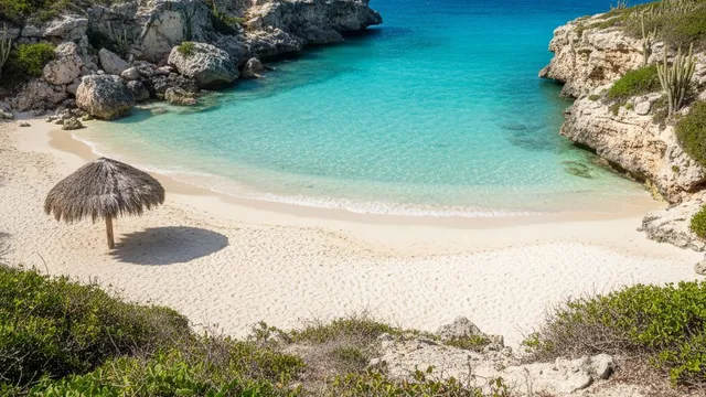 Kleine baai op Curaçao met helder turquoise water, wit zand en kalksteenrotsen met cactussen