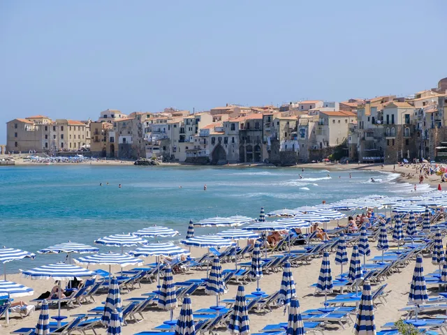 Blauw-witte parasols op het strand van Cefalù met de oude stad op Sicilië