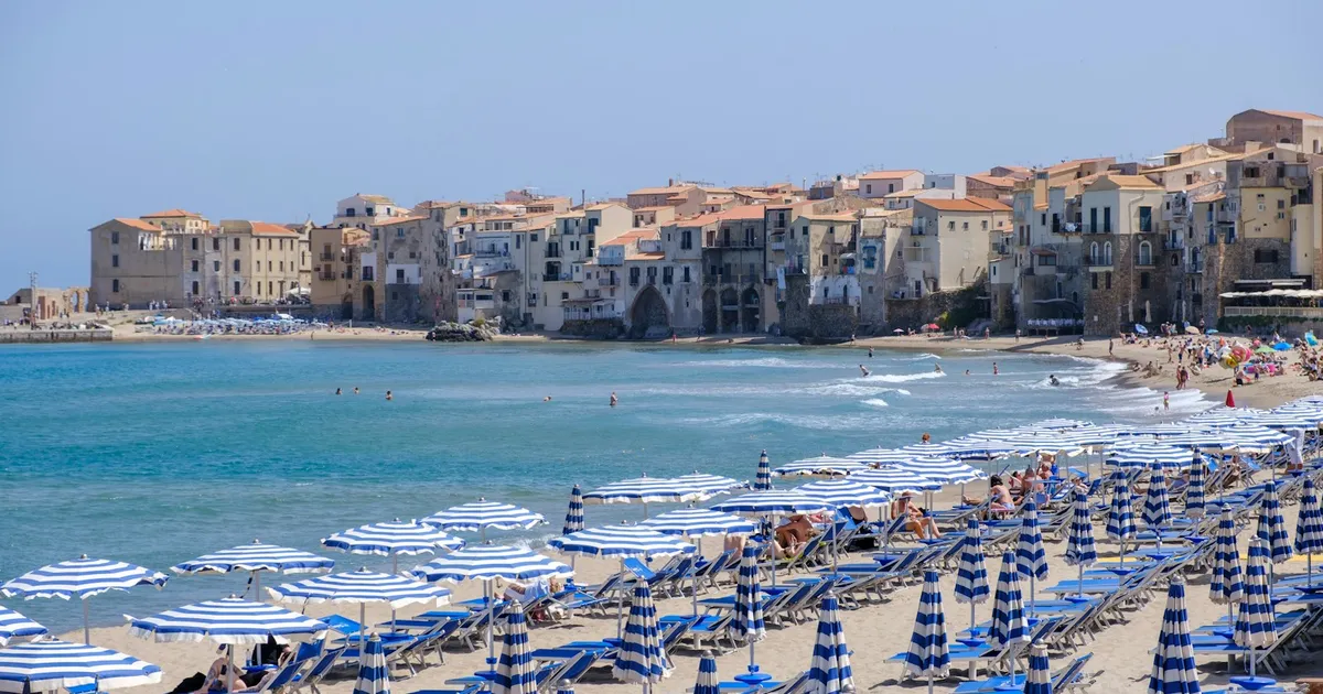 Blauw-witte parasols op het strand van Cefalù met de oude stad op Sicilië