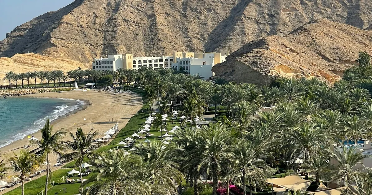 Resortbaai met palmen en ruige bergen aan de kust bij Muscat