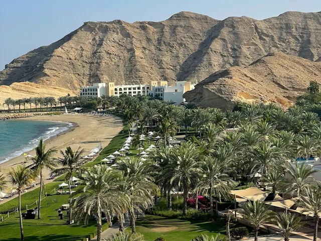 Resortbaai met palmen en ruige bergen aan de kust bij Muscat