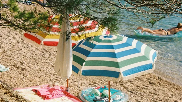 Kleurrijke parasols op een kiezelstrand aan helder zeewater
