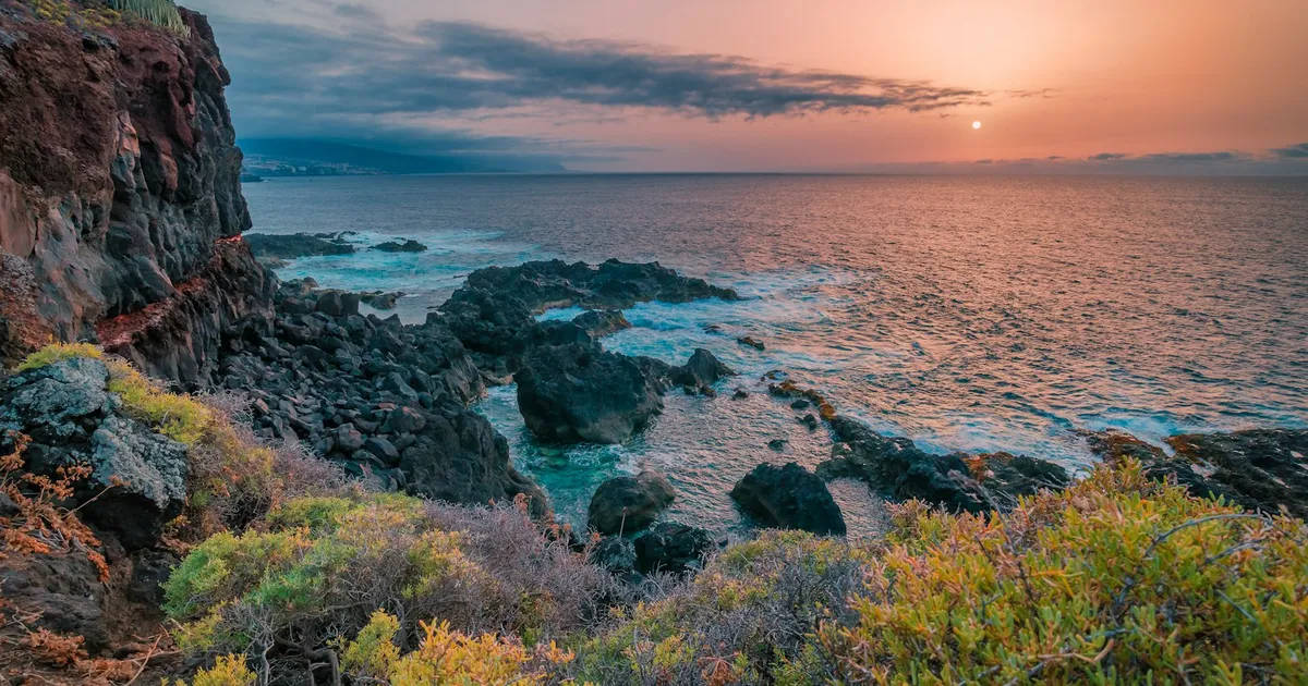 Rotsachtige kust van Tenerife met herfstkleurige struiken bij zonsondergang
