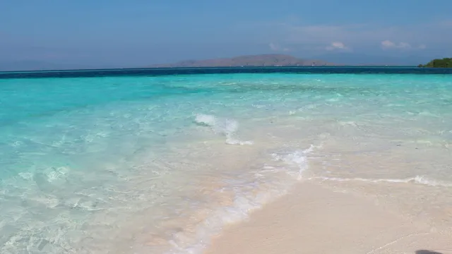 Helder ondiep zeewater langs een licht zandstrand onder een blauwe lucht