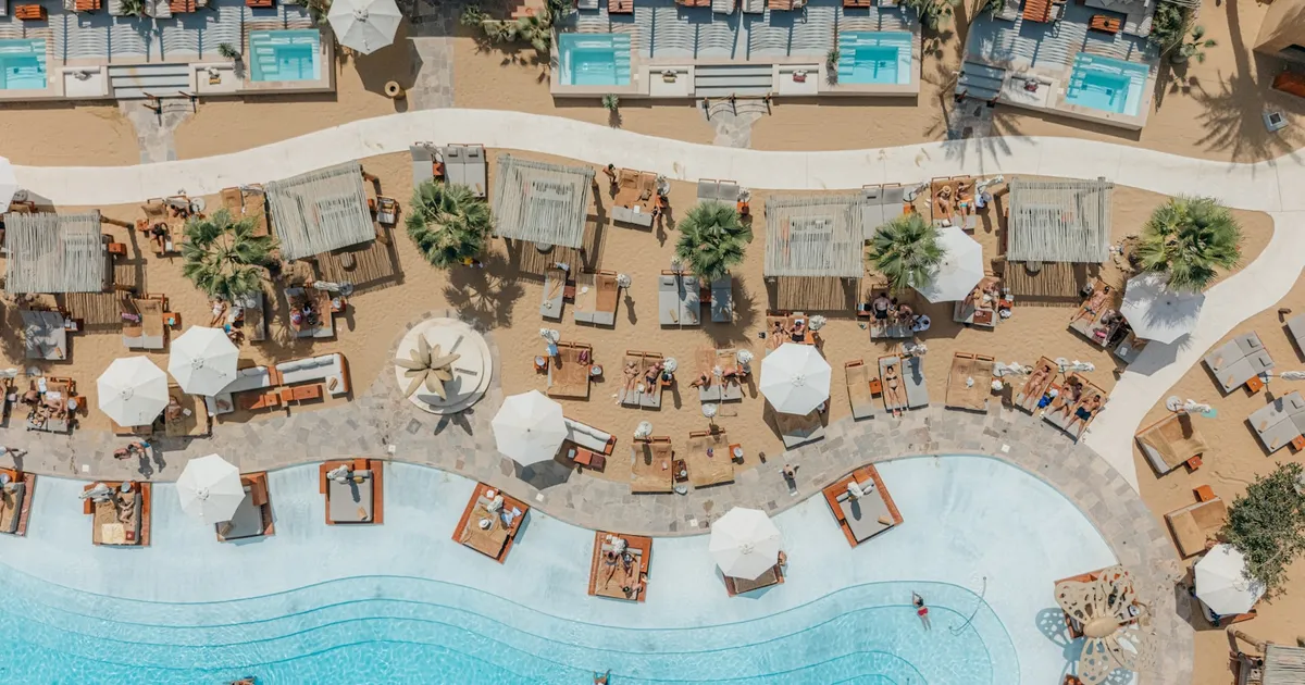 Luchtfoto van een resort met kronkelend zwembad, parasols en palmen